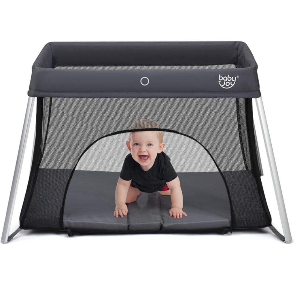 Best Travel Crib for Toddlers in 2026 Baby Joy Travel Crib with side-zip door and a smiling baby crawling inside the mesh playpen.