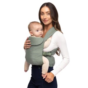 A woman in a white long-sleeved shirt and blue jeans, holding a baby in a sage green soft-structured baby carrier.